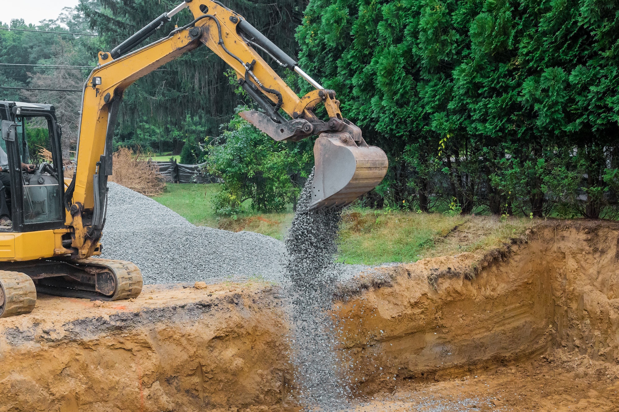 A yellow excavator bucket shovel moving gravel stones of foundation on a construction site stone